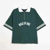 Chomba de piqué color verde con cuello polo blanco y cierre frontal parcial. Presenta un diseño holgado con mangas cortas que incluyen rayas blancas en los puños y un aplique frontal con el texto 'HOLE IN ONE' en color blanco.