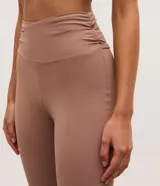 Pantalón deportivo de tiro alto con corte flare, confeccionado en microfibra elástica. Presenta un diseño ajustado en caderas y muslos con una apertura acampanada desde la rodilla y detalle de tajo lateral en el ruedo.