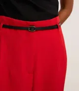 Pantalón de sastrería corte carrot, color beige, con cintura alta, pinzas frontales y cinturón fino incorporado con hebilla metálica.