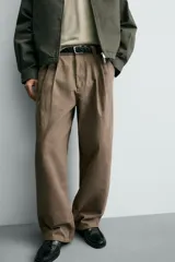 Pantalón de corte baggy fit confeccionado en tejido de algodón con estructura diagonal y efecto lavado. Presenta cintura con pliegues frontales, bolsillos laterales, bolsillos traseros de vivo y un bolsillo lateral adicional con doble vivo en la pernera. Cierre frontal con cremallera y botón.