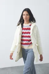 Campera capitoneada de largo medio en color crema, con cuello alto, cierre frontal y broches a presión. Presenta bolsillos laterales con solapa y diseño acolchado.