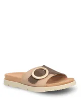 Sandalias tipo slide con tira ancha en tejido texturizado color beige y detalle de hebilla circular decorativa en tono marrón. Presentan una base ergonómica con suela de poliuretano ligera y flexible.