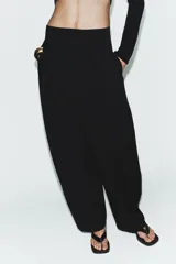 Pantalón negro de tiro alto, corte amplio estilo balloon o culotte, con pliegues marcados en el delantero y bolsillos laterales ocultos.