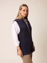 Chaleco de tejido de punto en color gris, con cierre frontal completo, cuello alto y dos bolsillos delanteros tipo parche.