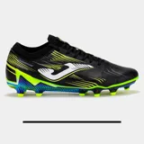 Championes de fútbol Joma modelo PCUW2501FG, color negro con detalles en amarillo neón, verde lima y azul iridiscente en la suela. Presentan un cuello de tejido elástico y el logo Joma en blanco.