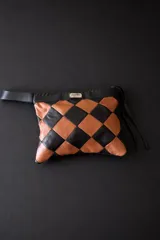 Cartera tipo sobre con diseño de ajedrez en rombos de cuero blanco y negro. Cuenta con una correa de mano integrada y detalle de placa metálica con logo.