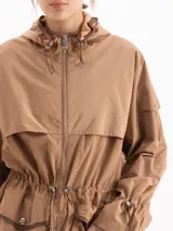 Piloto James de nylon liviano color marrón, con capucha envolvente, cintura ajustable con cordón y tancas, cierre frontal con cremallera y dos bolsillos delanteros con solapa y broches.