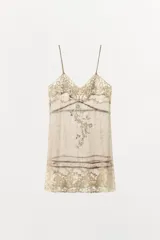 Vestido corto semitransparente de organza con escote en pico y tirantes finos. Presenta aplicaciones de bordados florales a contraste y detalles de cintas horizontales.
