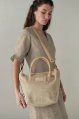 Cartera tipo tote bag confeccionada en lana fina sin teñir, con detalles de asas y correa regulable en cuero. Incluye cierre superior y forro interior.
