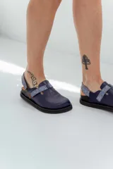 Zuecos de cuero azul con suela negra y tira trasera ajustable con hebilla.