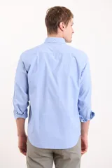 Camisa celeste con cuello abotonado, manga larga con puños abotonados y bolsillo en el pecho.