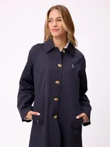 Gabardina de corte clásico en color azul marino, con cierre frontal de botones, cuello camisero y bolsillos laterales. Presenta un diseño minimalista con un pequeño bordado en el pecho.