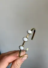 Pulsera rígida de bronce color dorado con tres piedras de ágata blancas de forma ovalada.