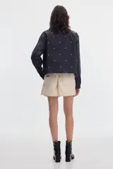 Camisa cropped de manga larga negra con estampado de lunares blancos, cuello camisero, cierre frontal de botones y bolsillos plaqué en el pecho.