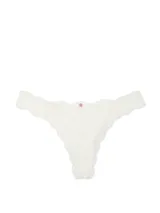 Panty tipo colaless confeccionada en encaje blanco con diseño floral, tiro bajo y detalle de pequeña roseta decorativa en la parte frontal.