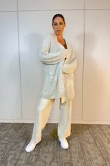 Sacón de punto largo en color beige, con diseño oversize, cuello redondo y mangas largas. Presenta una textura acanalada y un estilo abierto sin cierres.