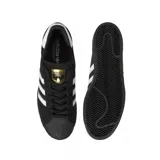 Championes adidas Superstar ADV, modelo clásico con puntera de goma, confeccionados en gamuza negra con las icónicas tres tiras laterales en blanco y detalle de logo dorado en la lengüeta.