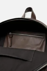 Mochila marrón oscuro de cuero, con compartimento principal con cierre de cremallera, bolsillo interno plano y bolsillo interno con cremallera. Bolsillo frontal con cremallera, parte posterior acolchada con banda de sujeción para equipaje, asa de mano y dos asas de hombro ajustables.