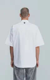 Camisa de manga corta en popelina de algodón, con silueta oversize y diseño funcional que incluye dos bolsillos delanteros, uno de ellos con solapa.