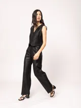 Pantalón de lino color beige, de tiro alto, pierna ancha y levemente acampanada. Tiene pinzas delanteras, elástico en la pretina trasera, cierre delantero y broche interno, bolsillos laterales y dobladillo invisible.