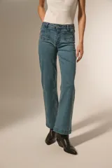 Pantalon de jean azul de corte recto, con bolsillos frontales decorados con tachas metálicas pequeñas y cintura con detalle de tachas a lo largo del borde superior.