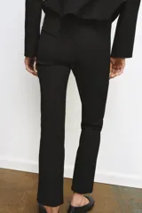Pantalón cropped negro de tiro alto, con cintura con trabillas y falsos bolsillos delanteros. Cierre frontal con cremallera, botón y ganchos metálicos.