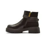 Bota corta de estilo urbano con suela track, confeccionada en una combinación de cuero liso y gamuza. Presenta una tira decorativa con hebilla metálica circular en el tobillo y elásticos laterales para facilitar el calce.