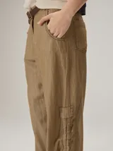 Pantalón de corte relajado color marrón, confeccionado en mezcla de algodón y lino. Presenta cintura con pasacintos, bolsillos laterales y diseño de botamanga ajustable con cordones y elástico.