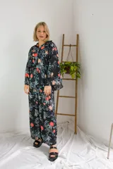 Pantalón largo de corte holgado con estampado floral en tonos rojos, naranjas, celestes y verdes sobre fondo negro.