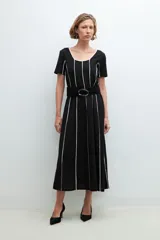 Vestido midi negro con rayas verticales blancas, escote redondo y cinturón negro con hebilla circular.