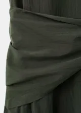 Vestido midi evasé color verde oscuro, sin mangas con tirantes anchos, cuello redondo y detalle de pañuelo cruzado en la cintura con lazo lateral. Cuenta con cierre de cremallera lateral.