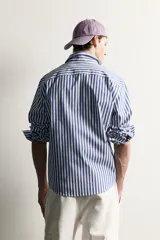 Camisa relaxed fit confeccionada en tejido de algodón, con diseño de rayas verticales en tonos azul y blanco, cuello con botones y manga larga.