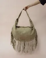Bolso tipo hobo de gran tamaño en color marrón, confeccionado en gamuza. Presenta un diseño con flecos largos en la parte inferior, cierre superior y una correa trenzada con detalles artesanales.