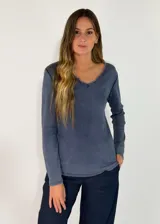 Remera de manga larga en color azul grisáceo con efecto lavado. Presenta un escote en V con detalle de borde deshilachado y costuras visibles.
