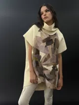 Poncho de lana merino afieltrada con cuello alto y mangas cortas. Diseño tipo mosaico con piezas geométricas en tonos verde azulado y gris.