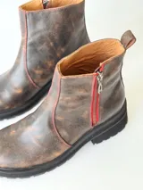 Botas cortas de cuero color chocolate, con elástico lateral, cierre interno con cremallera roja, pespuntes rojos y suela track.