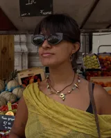 Collar corto de estilo artesanal, compuesto por una variedad de piedras naturales en tonos tierra, verdes, rojos y amarillos, intercaladas con pequeñas perlas de río. Presenta dijes de bronce macizo con formas orgánicas, incluyendo una figura de pez y un dije circular central, unidos por un cierre de barra y argolla.