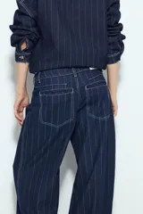Pantalón de jean de tiro bajo, color azul oscuro, con rayas verticales blancas y silueta ancha (wide leg). Presenta costuras contrastantes y dobladillo ancho doblado hacia afuera.
