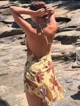 Vestido corto de tela liviana, color amarillo pálido con estampado de flores grandes en tonos marrones. Diseño halter con escote pronunciado en V y frunces en el torso y falda corta con ruedo asimétrico.