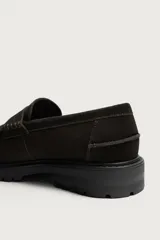 Mocasines de vestir color marrón oscuro, confeccionados en piel con acabado en gamuja serraje. Presentan detalle de antifaz en el empeine con costuras pespunteadas, punta redonda y suela track de goma robusta.