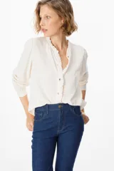 Camisa de manga larga color azul, con cuello mao y detalle de volados en la botonadura frontal. Presenta puños abotonados y un corte recto y fluido.