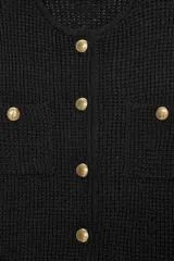 Chaqueta de punto texturizado color marrón oscuro, de corte cropped y cuello redondo. Presenta cierre frontal con botones dorados y dos bolsillos de plastrón decorativos con botón dorado en el pecho.