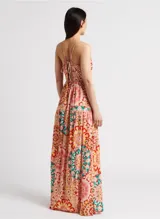 Vestido largo con estampado caleidoscópico en tonos rosa, rojo y verde. Presenta tirantes finos, escote en V, corte imperio y falda con volantes. Incluye detalle de trenzas en el pecho y la cintura que se anudan en la espalda descubierta.