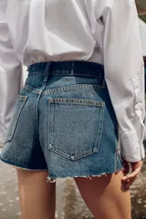 Shorts de jean tiro medio, corte mom fit, con bajo deshilachado y forro de bolsillos delanteros estampado a cuadros que asoma por debajo.