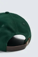 Gorra de seis paneles confeccionada en tejido de algodón, color verde oscuro, con parche frontal de letra P en color crema y ajuste posterior.