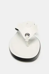 Sandalia plana de piel en color blanco, con diseño de dedo y detalle de aplique metálico. Presenta una suela plana en color negro.