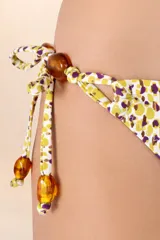 Calzón de bikini con estampado de manchas amarillas y violetas, con tiritas laterales ajustables adornadas con cuentas marrones.