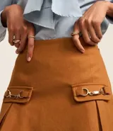 Minifalda marrón de polivelour con cierre lateral, solapas con hebillas y pliegues.