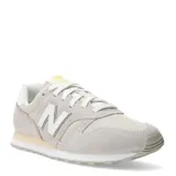 Championes urbanos New Balance modelo 373, color gris claro con detalles en beige y blanco. Confeccionados en una combinación de gamuza y malla, presentan el logo "N" característico en los laterales y una suela de goma con entresuela amortiguada.