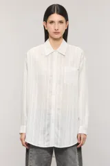 Camisa oversize de manga larga en color blanco con diseño de sutiles rayas verticales a tono y contratono, cuello camisero, bolsillo frontal en el pecho y cierre delantero con botones.